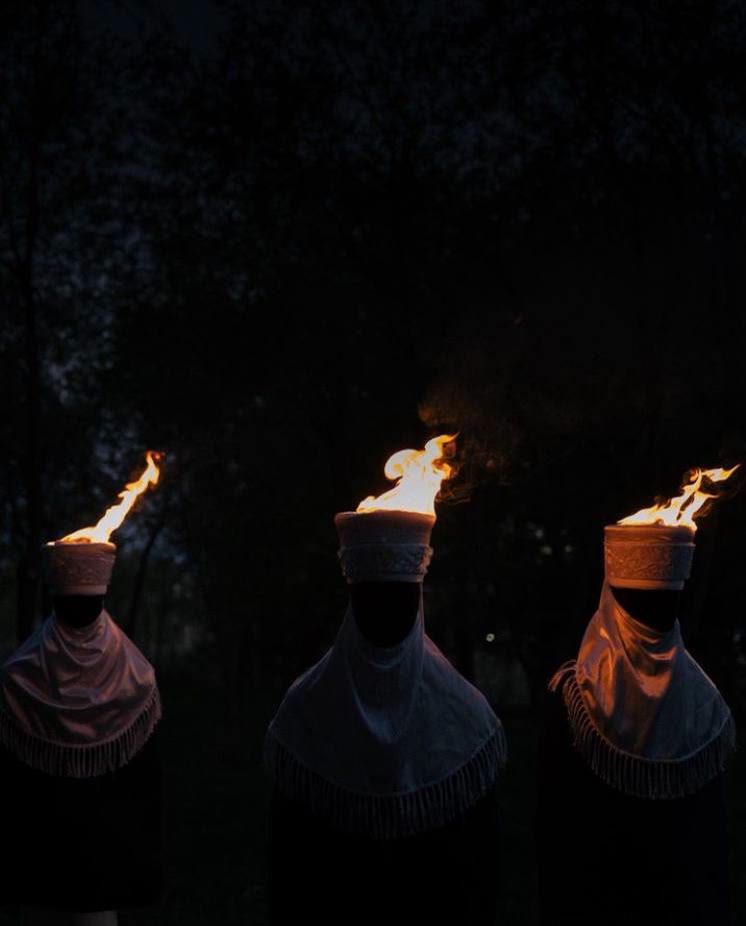 Qoorchaq — three veiled figures with burning headdresses at dusk